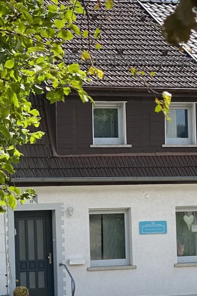 Ein Haus mit einem dunkelbraunen Dach und hellen Wänden, umgeben von Bäumen.