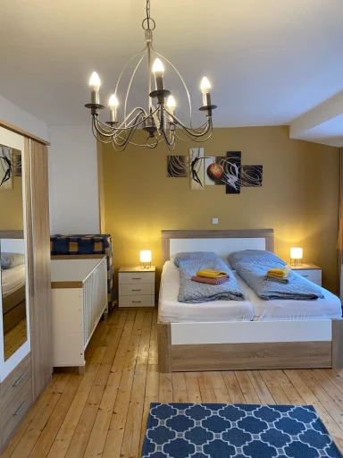Helles Schlafzimmer mit Doppelbett, Nachttischen, Spiegel und Kristalllüster.