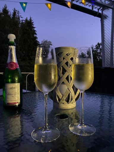 Zwei Gläser Sekt stehen auf einem Tisch, neben einer Flasche Sekt und einer laternenähnlichen Dekoration.