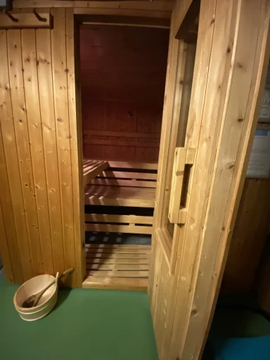 Holzsauna mit offener Tür und einem Eimer aus Holz daneben.