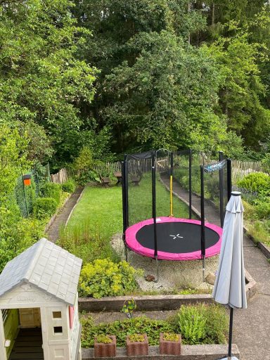 Ein Garten mit einem Trampolin und einem Spielhaus, umgeben von Bäumen und Pflanzen.
