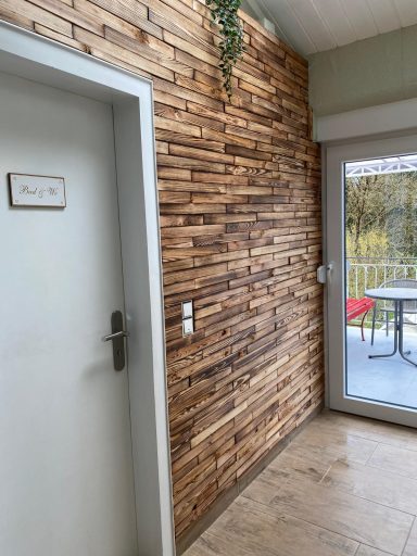 Holzwand mit gestreiftem Design, daneben eine Tür und ein Fenster mit Aussicht nach draußen.
